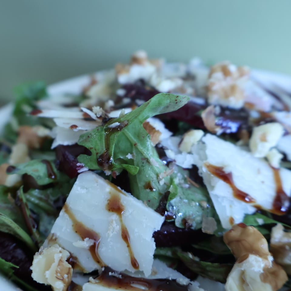 Close-up salad with leafy greens, crumbled white cheese, nuts, and balsamic drizzle.