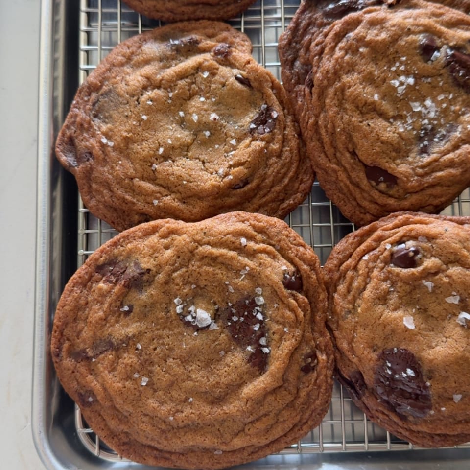 Close-up of oversized chocolate chip cookies sprinkled with flaky sea salt on a wire cooling rack.
