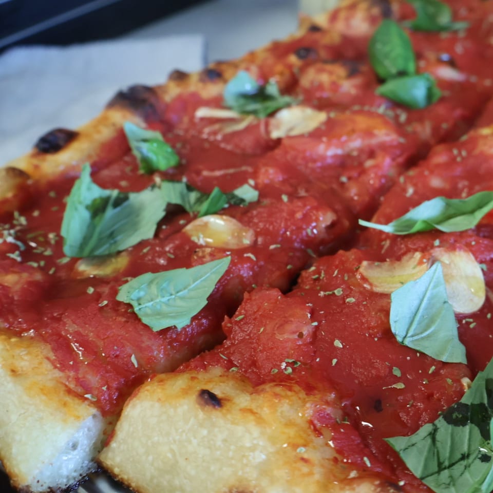 Close-up of a pizza topped with tomato sauce, basil leaves, garlic, herbs, and browned crust.