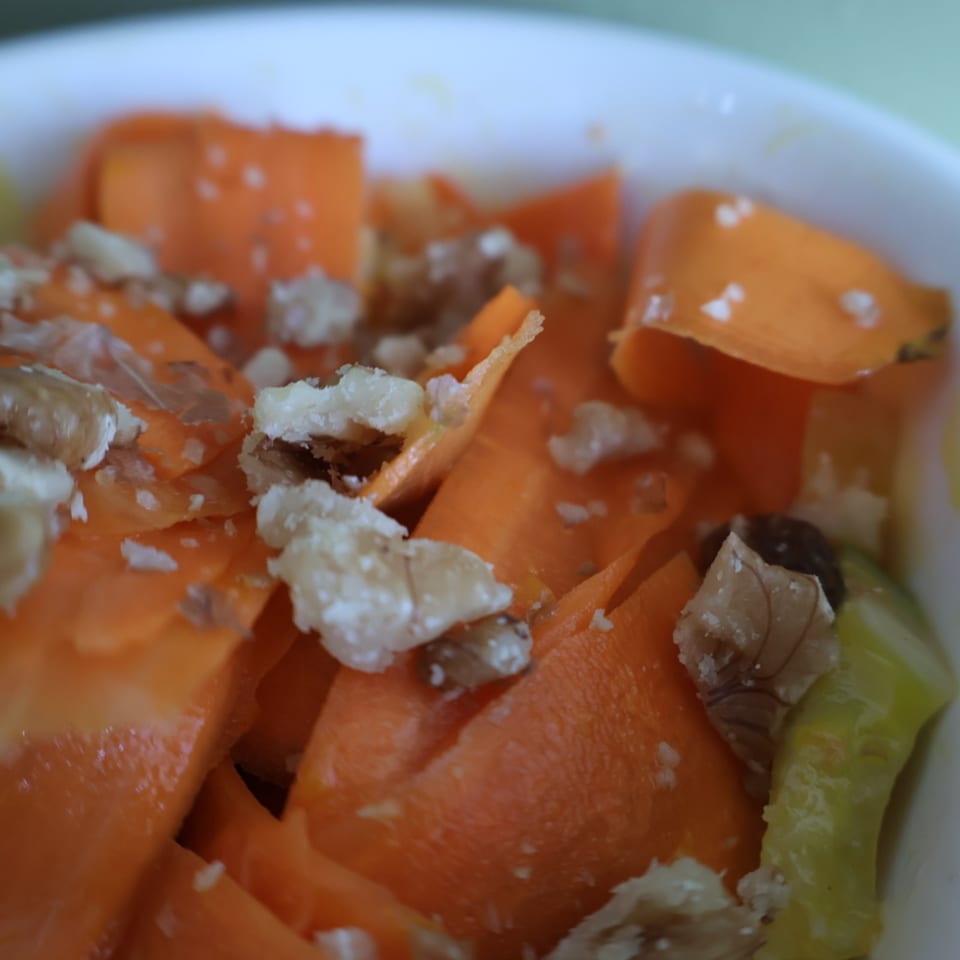 Close-up of orange vegetable pieces topped with crumbled white cheese, dark morsels, and green garnish.