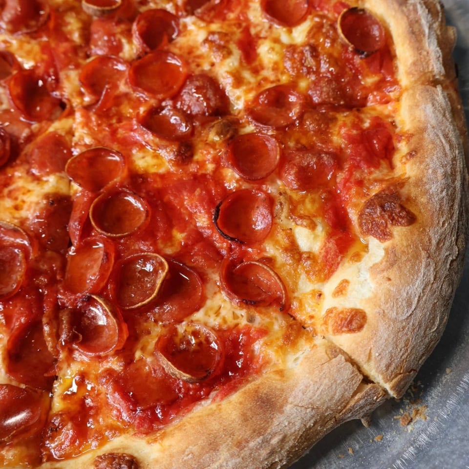 Close-up of a cheesy pepperoni pizza with abundant curled pepperoni slices and a golden, thick crust.